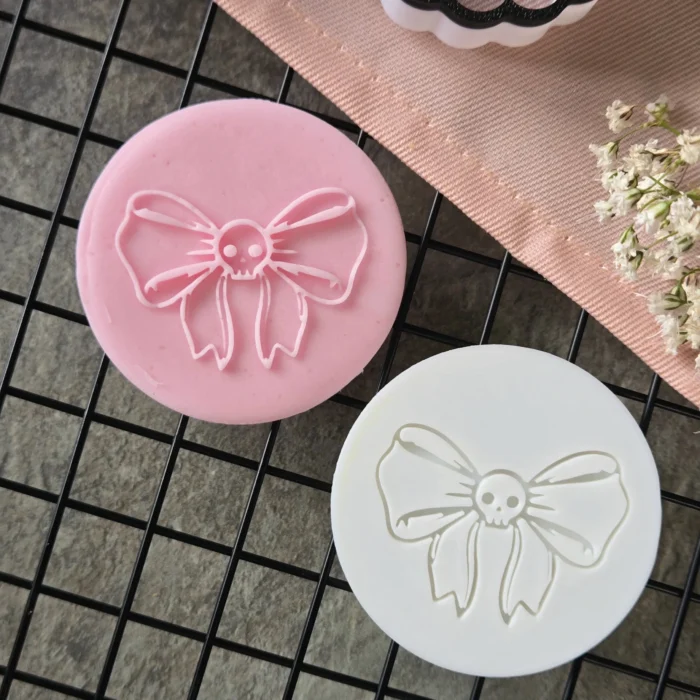 20250902_142450 Add a touch of goth glam to your Halloween sets. This round embosser presses a bow with a tiny skull—perfect for spooky favour boxes, treat bags and market trays. 3D-printed in the UK from eco-friendly PLA for crisp, even impressions.