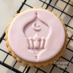 Pink fondant cookie with embossed mosque lantern and crescent moon design on a scalloped biscuit.